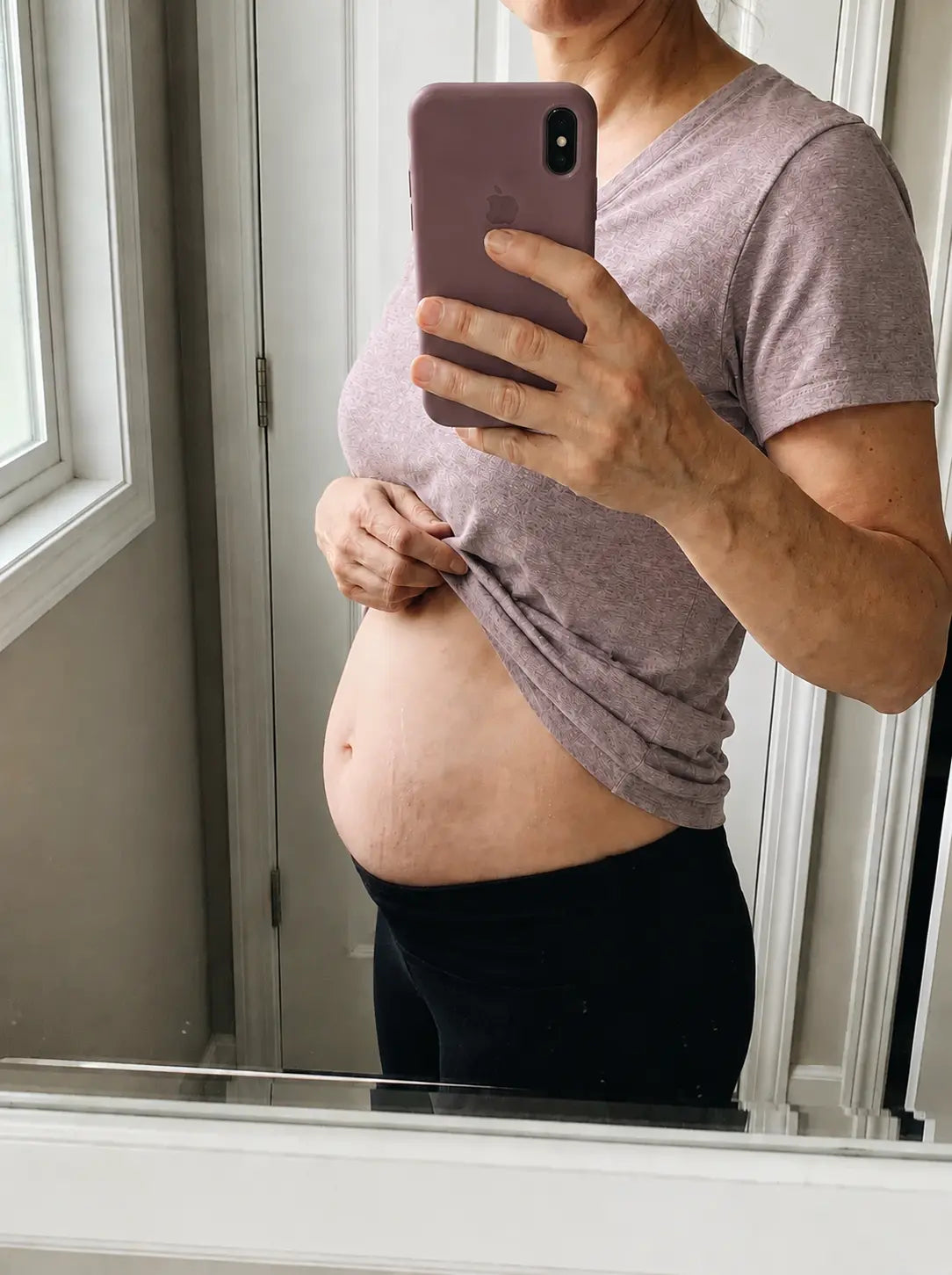 Femme de 45-50 ans devant un miroir, main posée sur le ventre, lumière naturelle, format 4:3